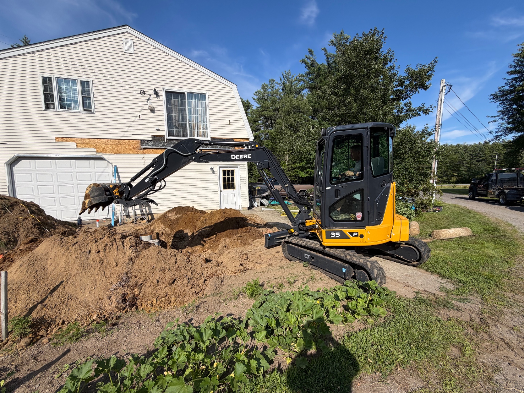 Nate's Septic John Deere 35 mini excavator digging beside a house and garage on a residential deck support install