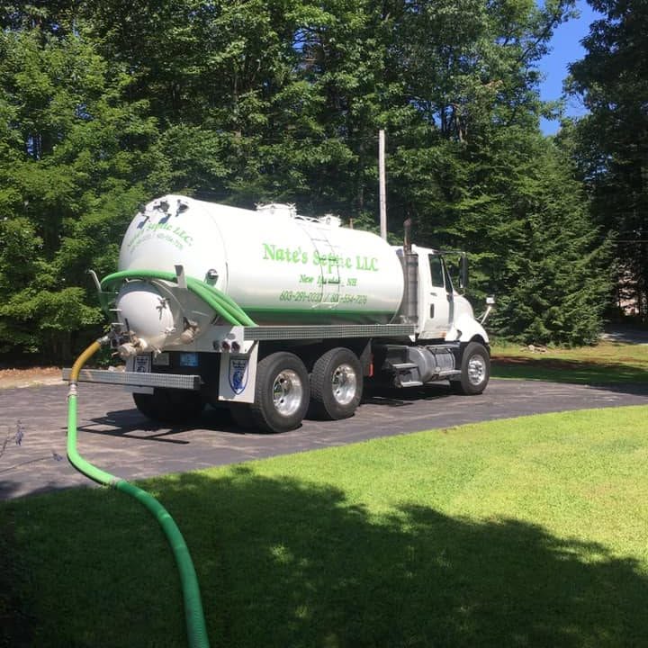 Nate's Septic pump truck on a paved driveway with a green suction hose running across the lawn during a tank pump-out